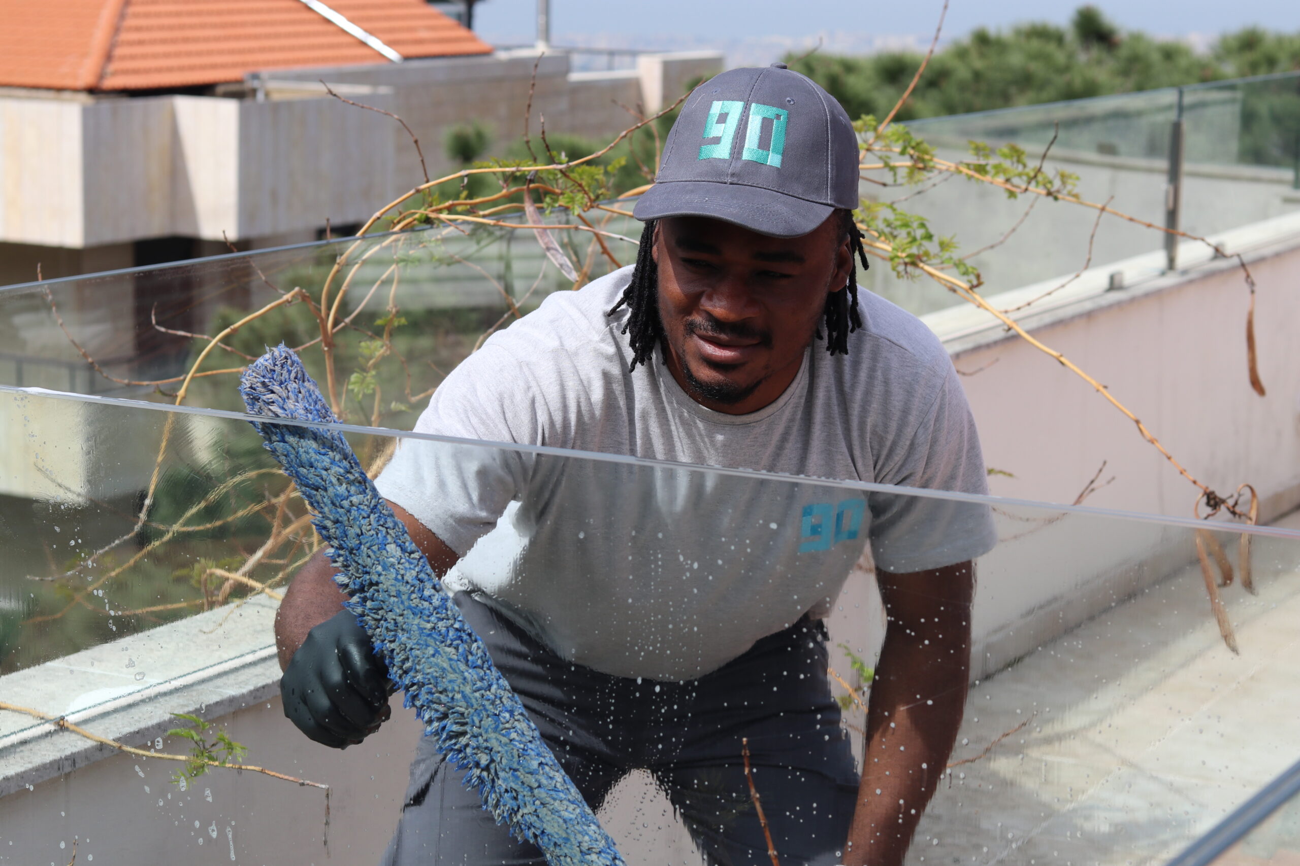 Nine Zero cleaner washing a glass balcony railing under sunlight during a window cleaning service in Lebanon.